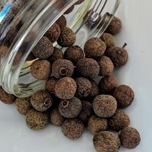 Allspice, Whole ~ Certified Organic in a jar on a white plate.