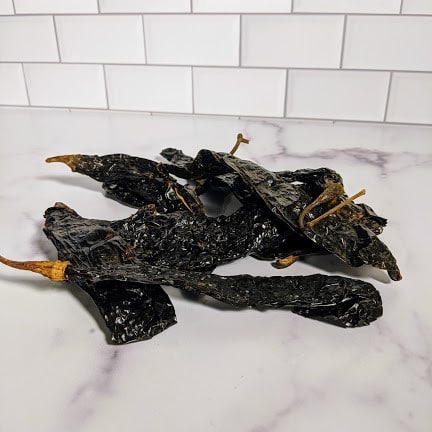 A Pasilla Negro Chiles - Whole sitting on top of a marble counter.
