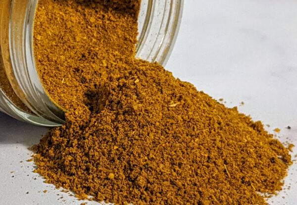 Certified Organic Jamaican Curry Powder displayed in a jar on a white surface.