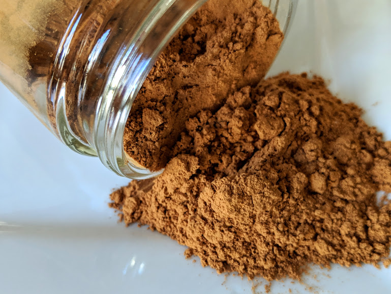 A jar of Cassia ~ Certified Organic cinnamon powder on a white plate.