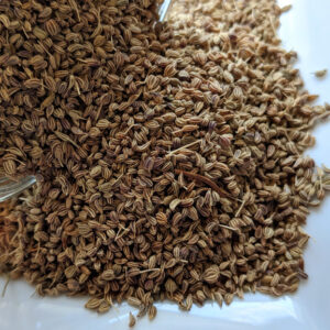 Ajwain seeds in a glass jar on a white plate.