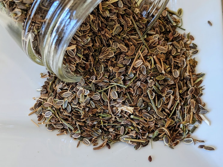 Dill seeds in a glass jar on a white plate.