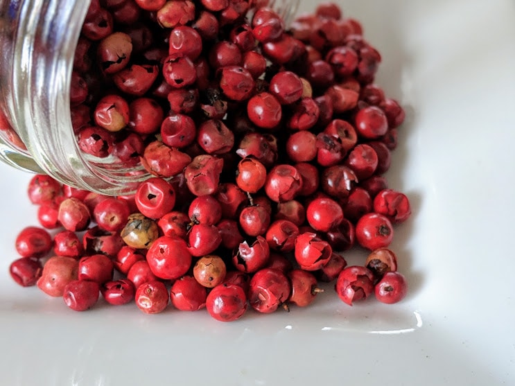 Pink peppercorns, Certified Organic, in a glass jar on a white plate.