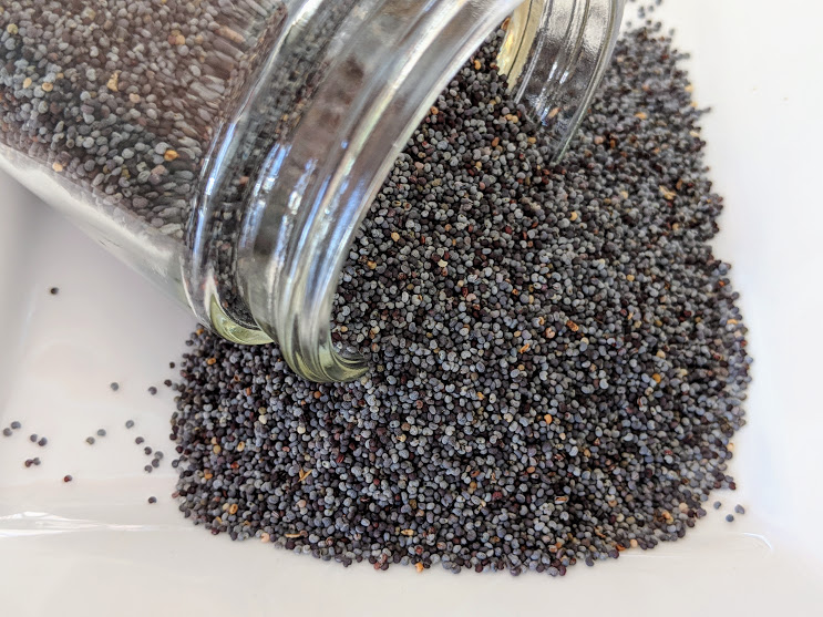 Poppy seeds in a glass jar on a white plate.